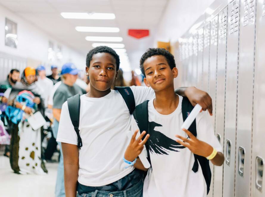 Two teen boys stand arm-in-arm in a school hallway with their new backpacks during Utah Refugee Connection’s Back to School event.