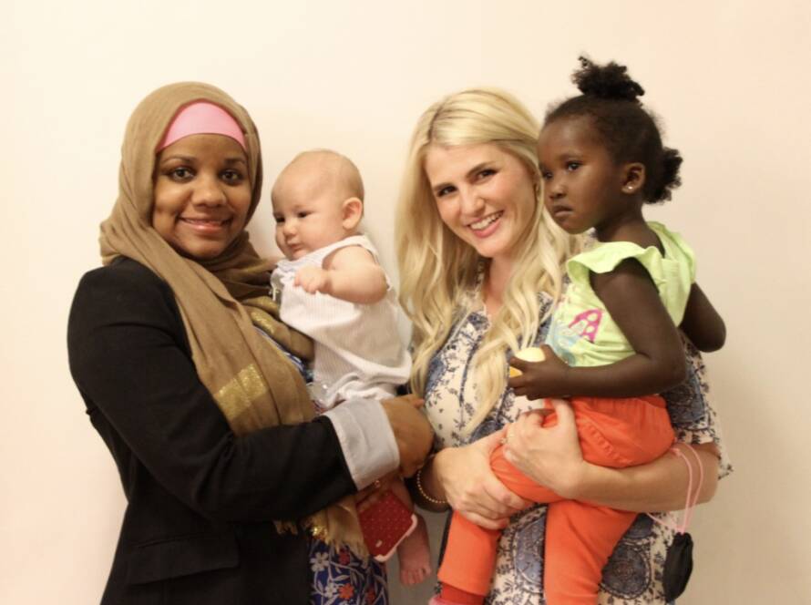 Two mothers hold their young children while standing together, reflecting the supportive connections Utah Refugee Connection builds with refugee families as they find safety, belonging, and hope in Utah.