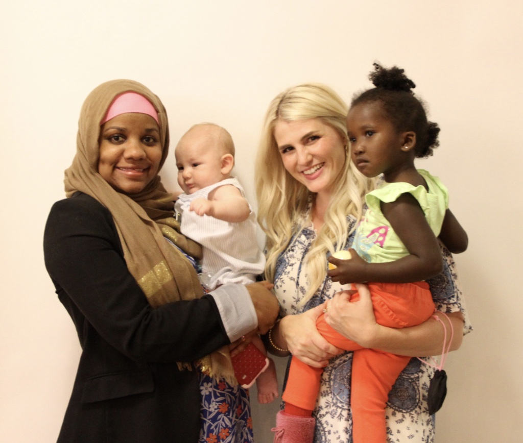 Two mothers hold their young children while standing together, reflecting the supportive connections Utah Refugee Connection builds with refugee families as they find safety, belonging, and hope in Utah.