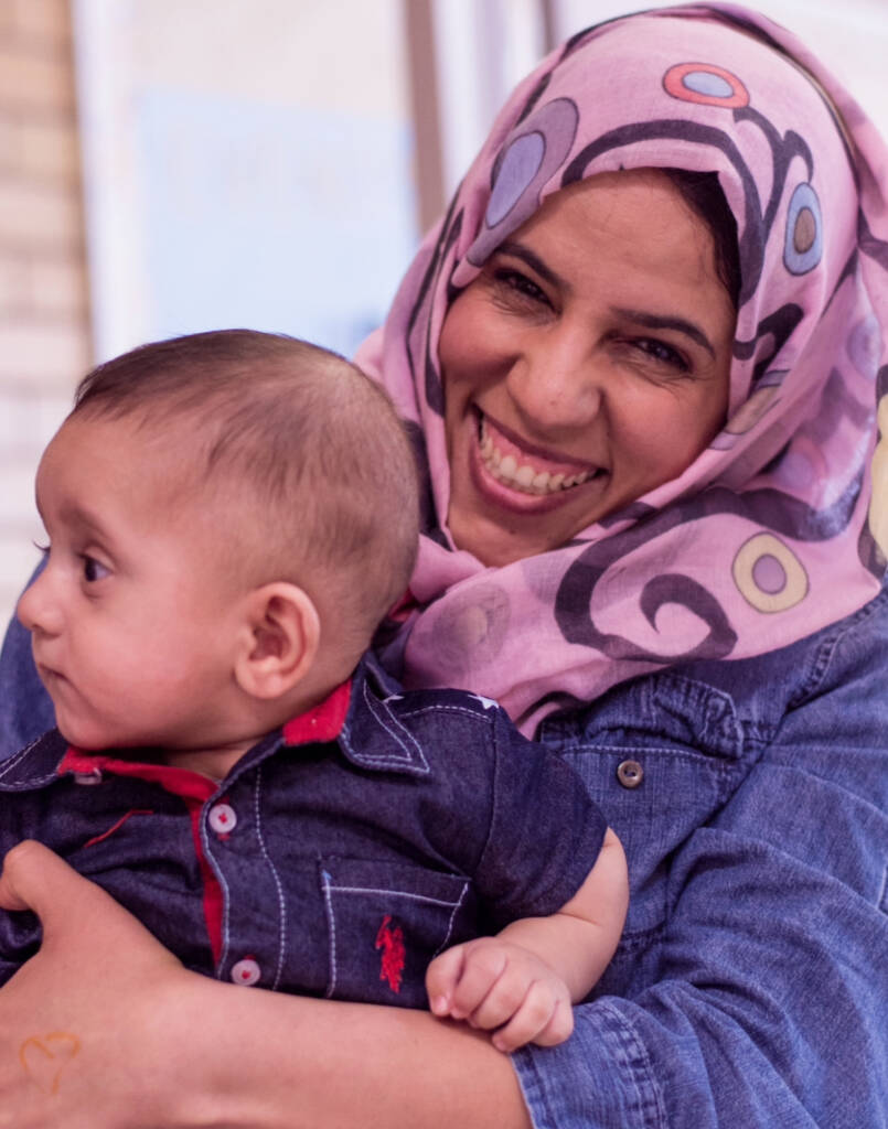 A refugee mother smiles while holding her baby during a Utah Refugee Connection gathering in Utah. Utah Refugee Connection supports refugee mothers and families through community connection, maternal resources, and family support programs.